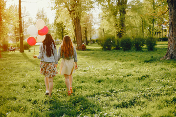 two young and bright girls spend their time in the summer park with balloons