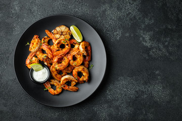 Grilled shrimps or prawns served with lime, garlic and white sauce on a dark concrete background....