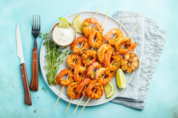 Grilled shrimp skewers or langoustines served with lime, garlic and sauce on a light blue concrete...