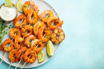 Grilled shrimp skewers or langoustines served with lime, garlic and sauce on a light blue concrete background. Seafood and beer. Top view with copy space. Flat lay