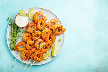 Grilled shrimp skewers or langoustines served with lime, garlic and sauce on a light blue concrete background. Seafood and beer. Top view with copy space. Flat lay