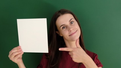 Portrait of beautiful smiling female wearing red t-shirt, posing with white blank paper with copy space for your advertisement information and looking at camera, against green background.