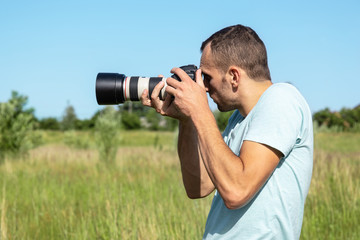 Fototapeta na wymiar young male photographer with big professional camera on nature background