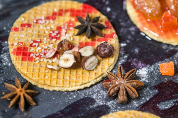 Sweet dessert on dark background. Traditional breakfast with gaufre, waffle, crispy wafer with nuts, fruits and syrup.