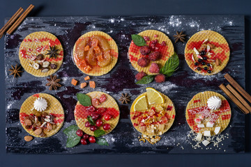 Sweet dessert on dark background. Traditional breakfast with gaufre,  waffle, crispy wafer with berries, nuts, fruits and syrup.