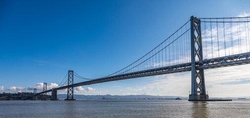 San Francisco bay bridge stretching into the distance with very clear blue sky and light clouds in...