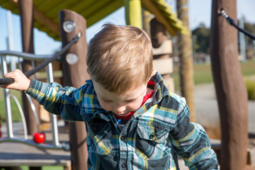 A little boy carefully practices walking across the swing bridge on the playground fort 