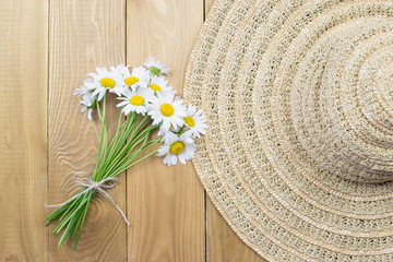 Straw hat, bouquet of daisies on a wooden background, top view. Copy Space. The concept of summer fashion. Vacation, weekend, summer.