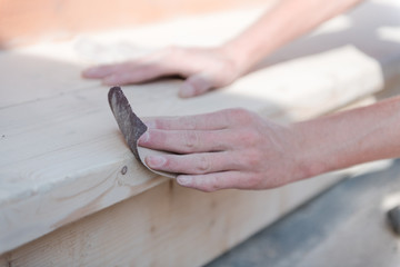 Sand the wood with sandpaper. A man polishes a tree. Work with sandpaper. To make wooden products. Make boards smooth.