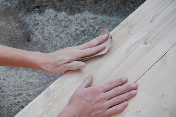 Sand the wood with sandpaper. A man polishes a tree. Work with sandpaper. To make wooden products. Make boards smooth.