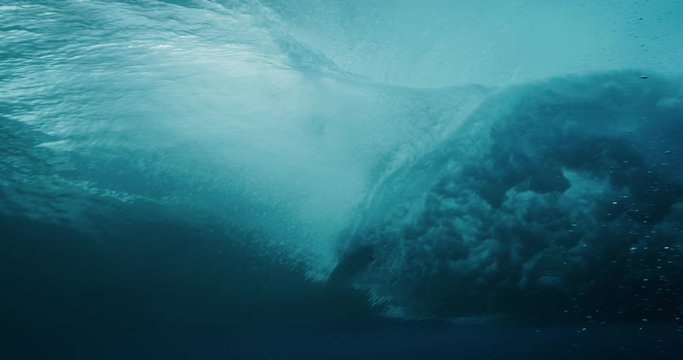 Underwater shot of a breaking wave with a surfboard silhouette riding over the oceans blue surface