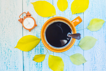 Fototapeta na wymiar Autumn background. Coffee mug on a blue Board background with yellow falling leaves and cones. Hello autumn. Flat lay composition of the drink in an even layer.