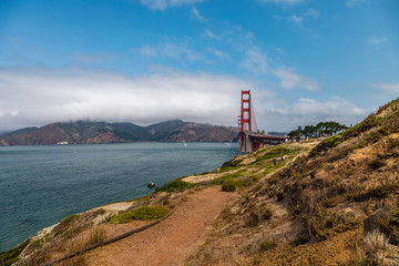 Fototapeta na wymiar Golden Gate Bridge on the right with calm water from the San Francisco Bay on the left and a dirt footpath in the foreground
