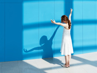 Fototapeta na wymiar Beautiful Chinese brunette woman in white wedding dress dancing with her shadows on blue wall background. Sunny portrait of glamour young stylish lady. Emotions, beauty and lifestyle concept.