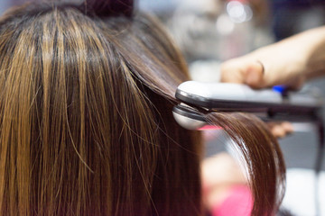 Fototapeta premium Hairdresser using hair straightener on brown-haired woman