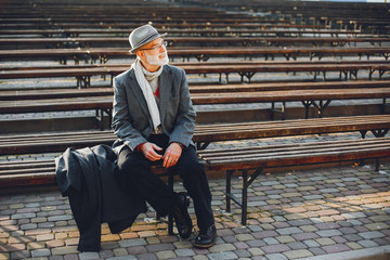 Handsome grandfather in a autumn park. Old man in a gray jacket and hat. Male sitting on the bench