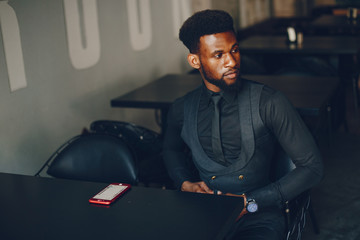 A young and handsome dark-skinned boy in a black suit sitting in a cafe