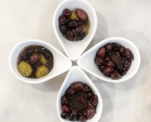 Top down view of marinated olives in four modern white bowls.