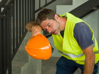 Portrait of attractive and exhausted construction worker in helmet and vest at building site taking a breath during a hard working day all sweaty and tired