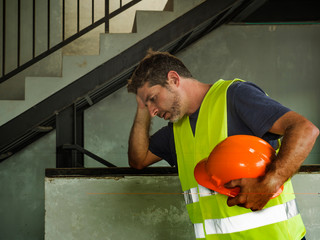 . Attractive stressed and frustrated construction worker man in vest and builder helmet looking tired and worried suffering problem in blue collar job lifestyle concept