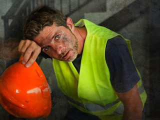Portrait of attractive and exhausted construction worker in helmet and vest at building site taking...