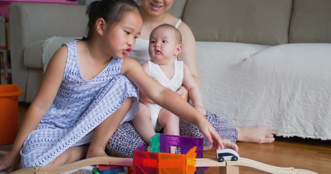 little asian girl playing building blocks game on the floor at home with her mother holding little baby sister beside  asian family lifestyle with two kids