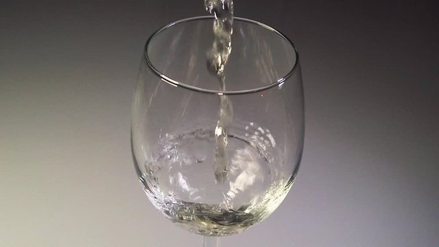 Long close-up shot of white wine being poured into a wine glass in slow motion.