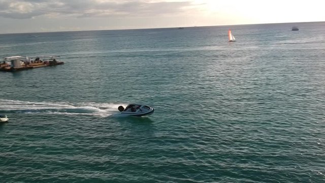 Aerial shot focused on a sports boat pulling a donut float with people on it, ath sunset in a paradise island.