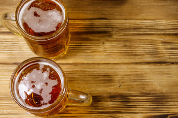 Two mugs of beer on a wooden table. Top view, copy space