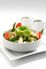 Fresh and healthy cesar salad on white tableware, with tomatoes, avocado, lettuce, asparagus and chicken