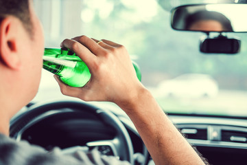 Drunk man driving a car on the road holding bottle beer Dangerous drunk driving concept