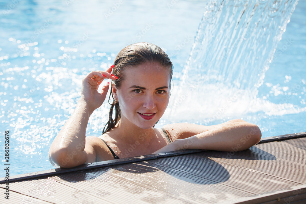 Canvas Prints Young beautiful woman under a waterfall in a pool with clear blue water.