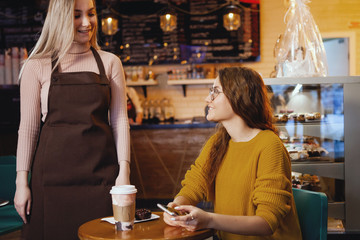 Young pretty woman and waitress in cafe.
