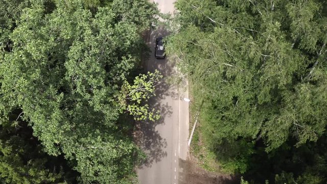 Drone view black car moving on countryside highway on green forest background. Aerial view japanese car riding on asphalt road. Summer travel on car