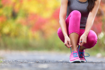 Autumn running shoes girl tying laces ready to run in forest foliage background. Sport runner woman...