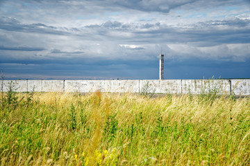 Fototapeta premium Lighthouse or old beacon under storm clouds against yellow field