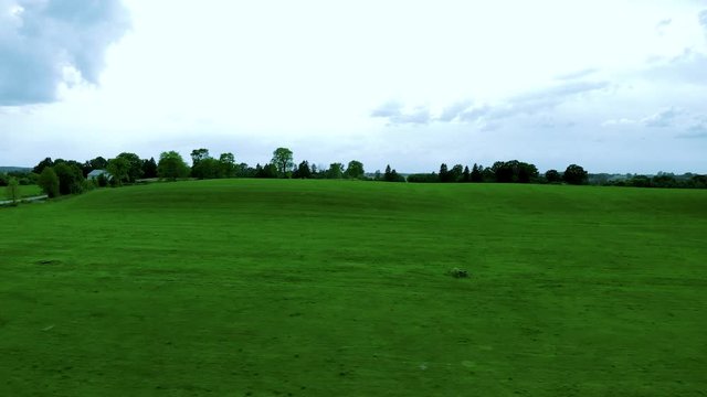 Aerial footage over grass field, green lawn and blue sky, natural landscape on village, cinematic image shot by drone