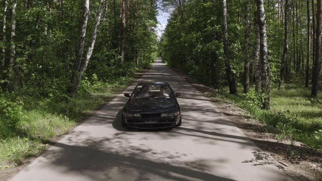 Car moving on countryside road through birch grove. Aerial view japanese low car driving on country highway past green birch forest. Car trip at summer vacation