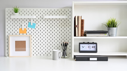 Workspace pegboard and shelves with office supplies on white office desk.