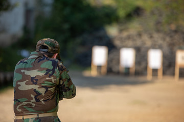 a guy in army clothes shoots at a target with a submachine gun