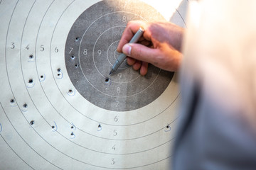 a man in a suit marks with a pen the impact of bullets on a target