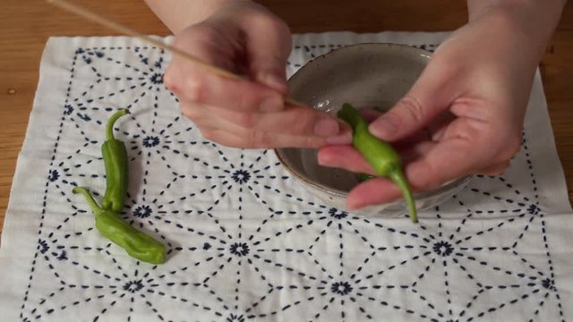 a Japanese female chef making holes on sweet green peppers at her home kitchen, Tokyo, Japan. June 2019. Camera fixed, close-up, high angle