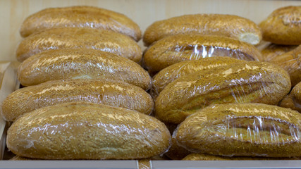 Loafs of fresh grain bread wrapped in polyethylene on a pallet with fresh bread