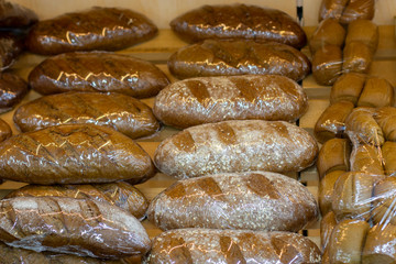 Loafs of fresh rye bread in flour sprinkles wrapped in plastic film on a bakery counter