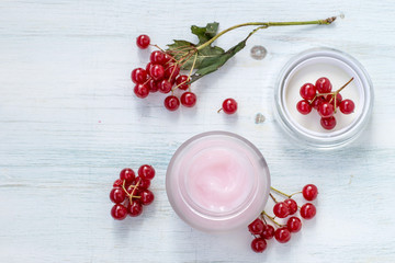 Cosmetics for face and body skin care. Jar with cream and fresh berries of viburnum on a light wooden background. Selective focus.