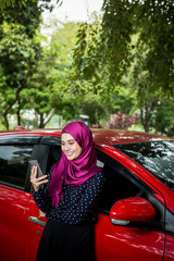 Happy Muslim Lady with her smartphone next to her car. Insurance Claim success concept.