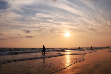 Silhouette of people playing in to the sea with dramatic sunset sky
