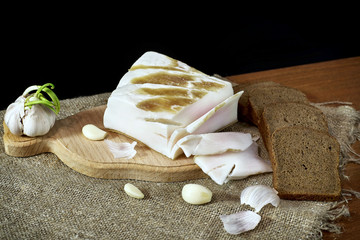 Bread lard and garlic on wooden board against burlap background