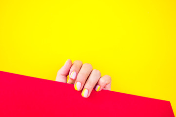 Young woman's hand with beautiful manicure on bright yellow background holding red color paper.