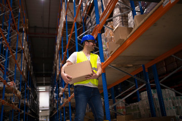 Warehouse male worker relocating packages and putting boxes on shelf in large storage distribution center.